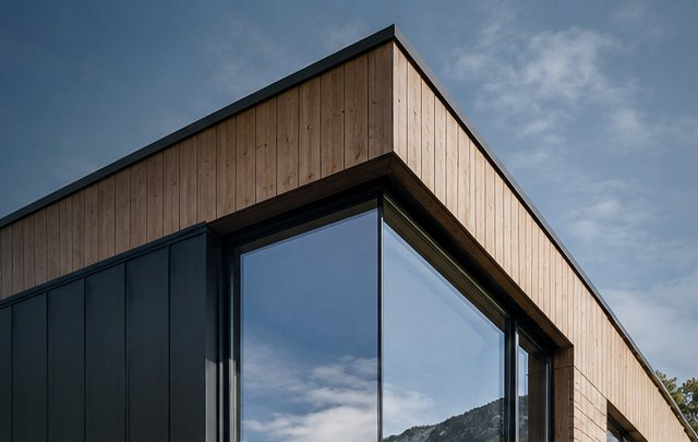 Esquina de una vivienda con revestimiento de madera y ventanales, bajo cielo de montaña